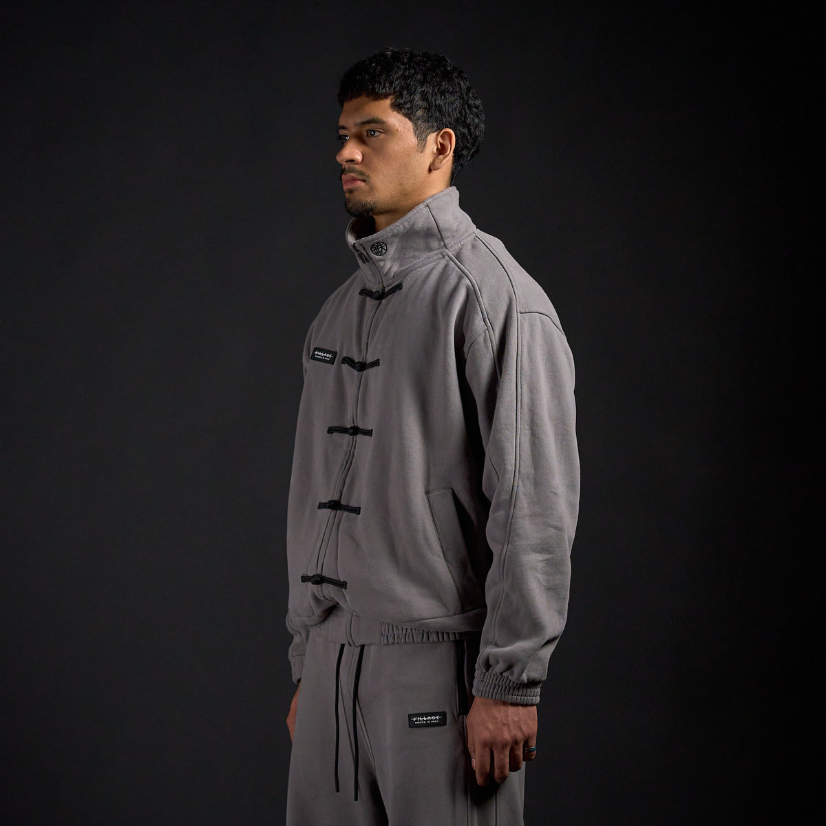 Tang Warmup Jacket in DARKSIDE charcoal grey, three-quarter view on model | Village Hidden in Iron