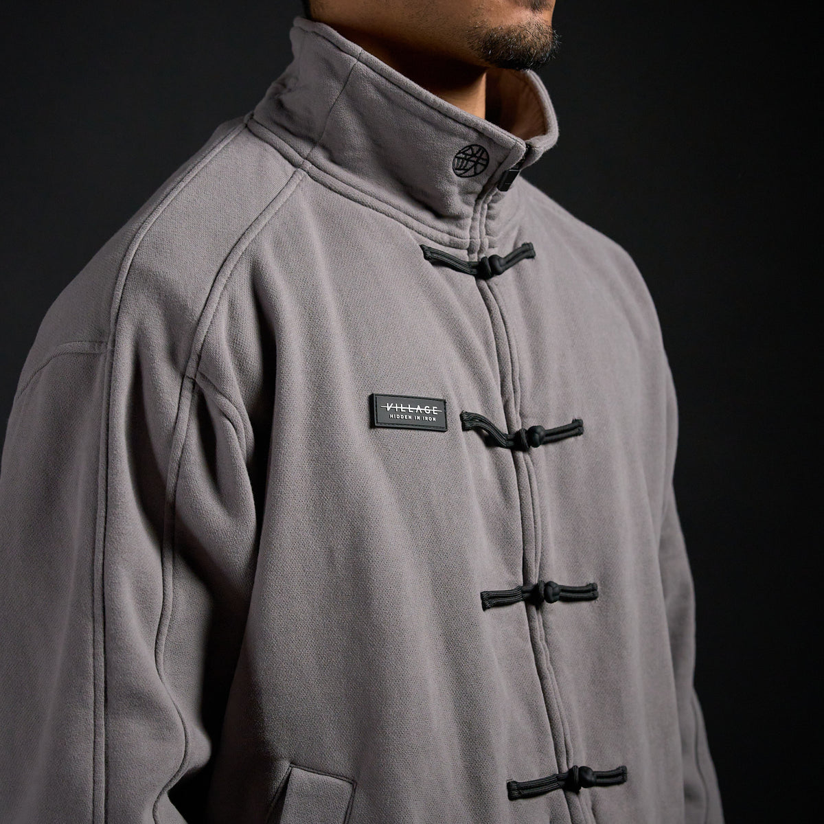 Tang Warmup Jacket in DARKSIDE charcoal grey, close-up of stand collar and frog closures | Village Hidden in Iron